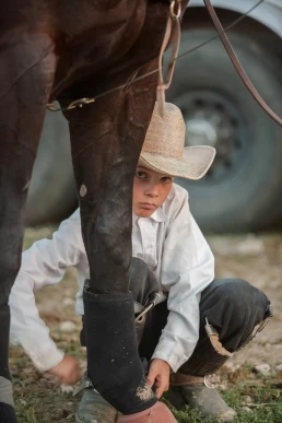 A boy kneeling next to a horse.