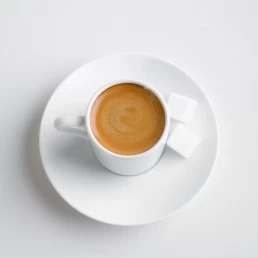 A cup of coffee with sugar on a saucer for a Food Photography shoot, on a white background.