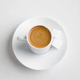 A cup of coffee with sugar on a saucer on a white background for a company headshot.