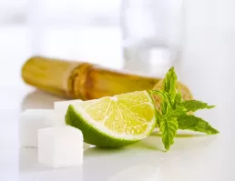 A lime, sugar, and a bamboo stick on a white surface for food photography.