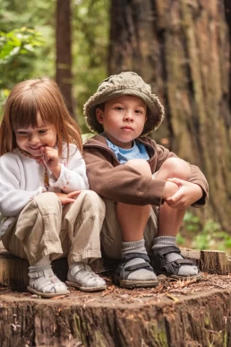 Two children sitting on a tree stump in the woods, posing for a healthcare photography session.