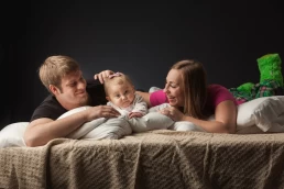 A family laying on a bed with a baby, captured in a healthcare photography style.