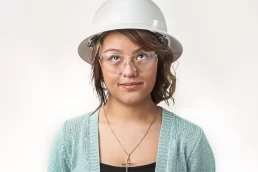 A young woman wearing a hard hat and glasses for her company headshot.