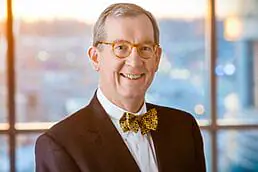 A man in a suit and bow tie smiling in a healthcare photography setting in front of a window.
