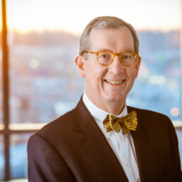 A man in a suit and bow tie smiling in a healthcare photography setting in front of a window.