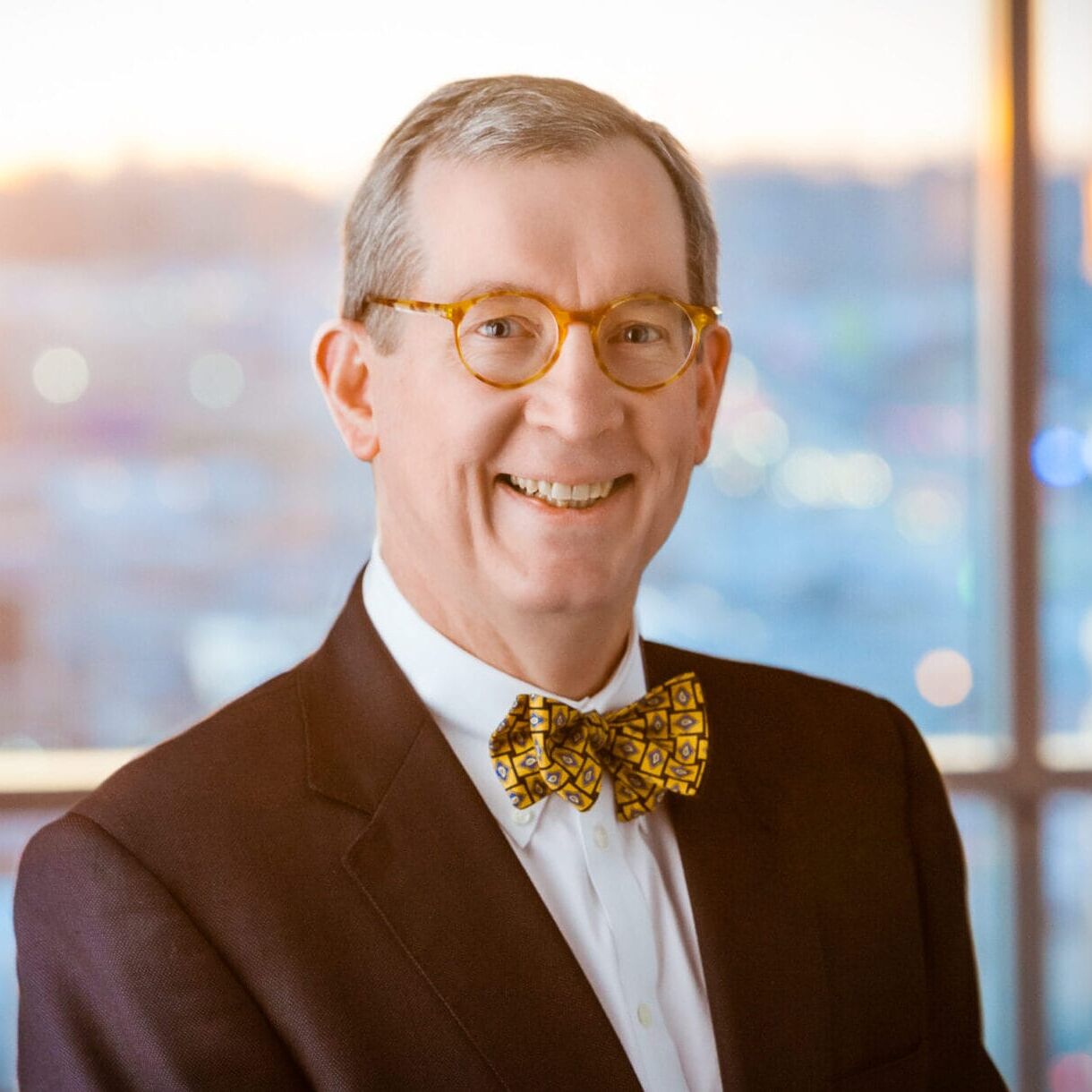 A man in a suit and bow tie smiling in a healthcare photography setting in front of a window.