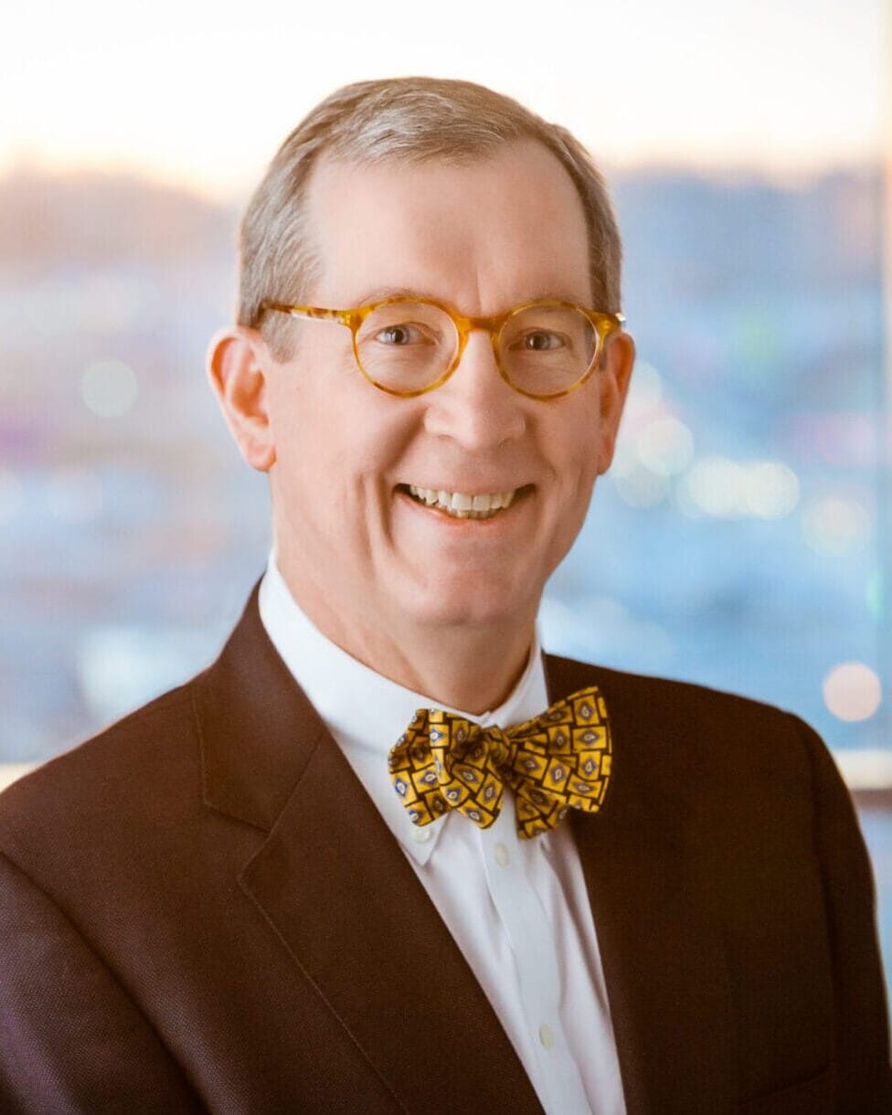 A man in a suit and bow tie smiling in a healthcare photography setting in front of a window.