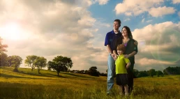 A family is standing in a field with the sun behind them for a company headshot.