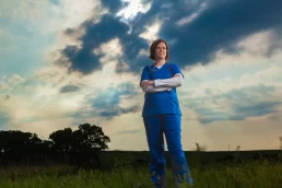 A nurse standing in a field under a cloudy sky for a company headshot.