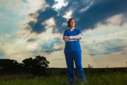 A nurse standing in a field under a cloudy sky for a company headshot.