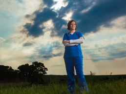 A nurse standing in a field under a cloudy sky for a company headshot.