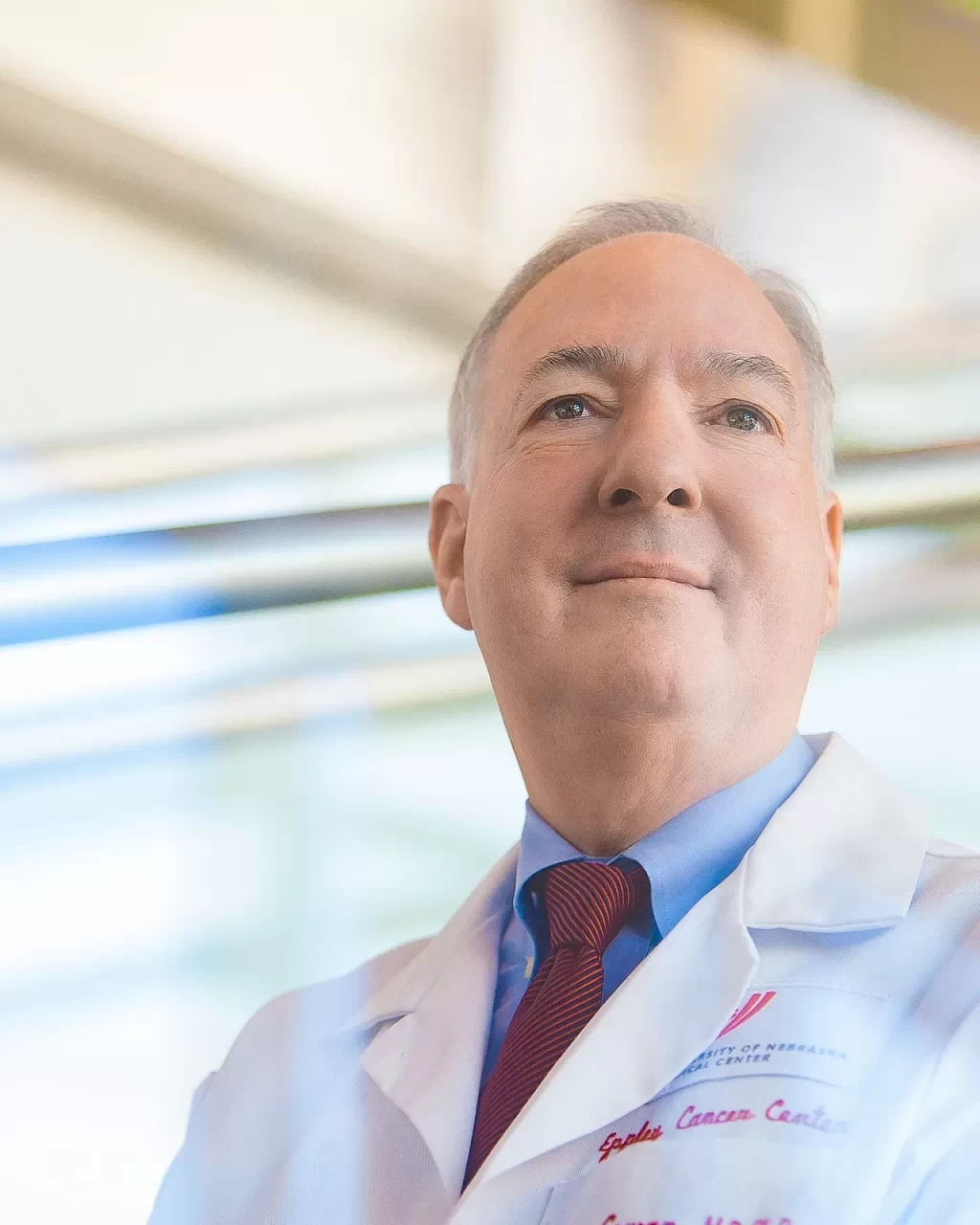 A man in a lab coat is standing in front of a glass wall for his healthcare photography headshot.