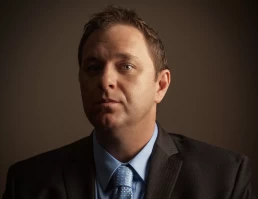 A man in a suit and tie looking at the camera for his company headshot.