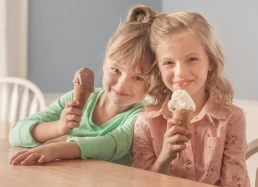 Two girls holding ice cream cones at a table for a company headshot.