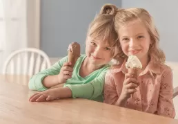 Two girls holding ice cream cones at a table for food photography.