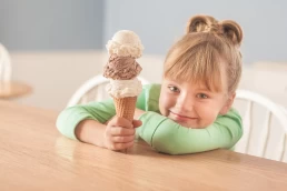 A little girl holding three ice cream cones at a table for a healthcare photography session.