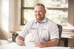 A man sitting at a desk with a hard hat for a company headshot.