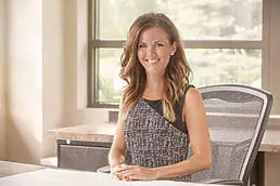 A woman sitting at a desk in an office for her company headshot.
