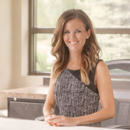 A woman sitting at a desk in an office for her company headshot.