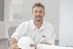 A man wearing a white hard hat and holding a company headshot.