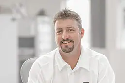 A company headshot of a man in a white shirt sitting at a desk.