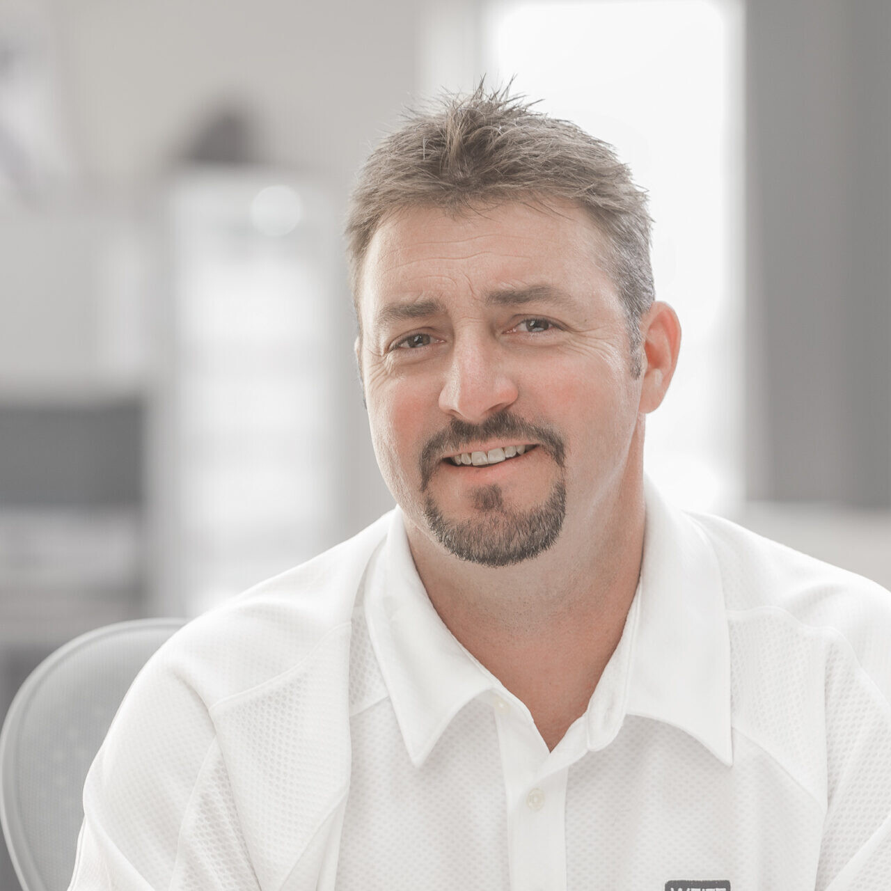 A company headshot of a man in a white shirt sitting at a desk.