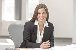A woman in a business suit sitting at a desk for her company headshot.