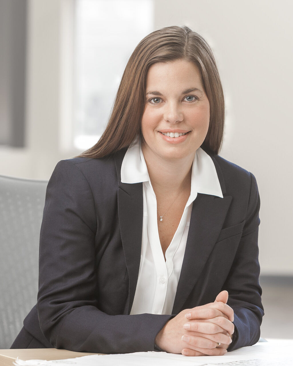 A woman in a business suit sitting at a desk for her company headshot.
