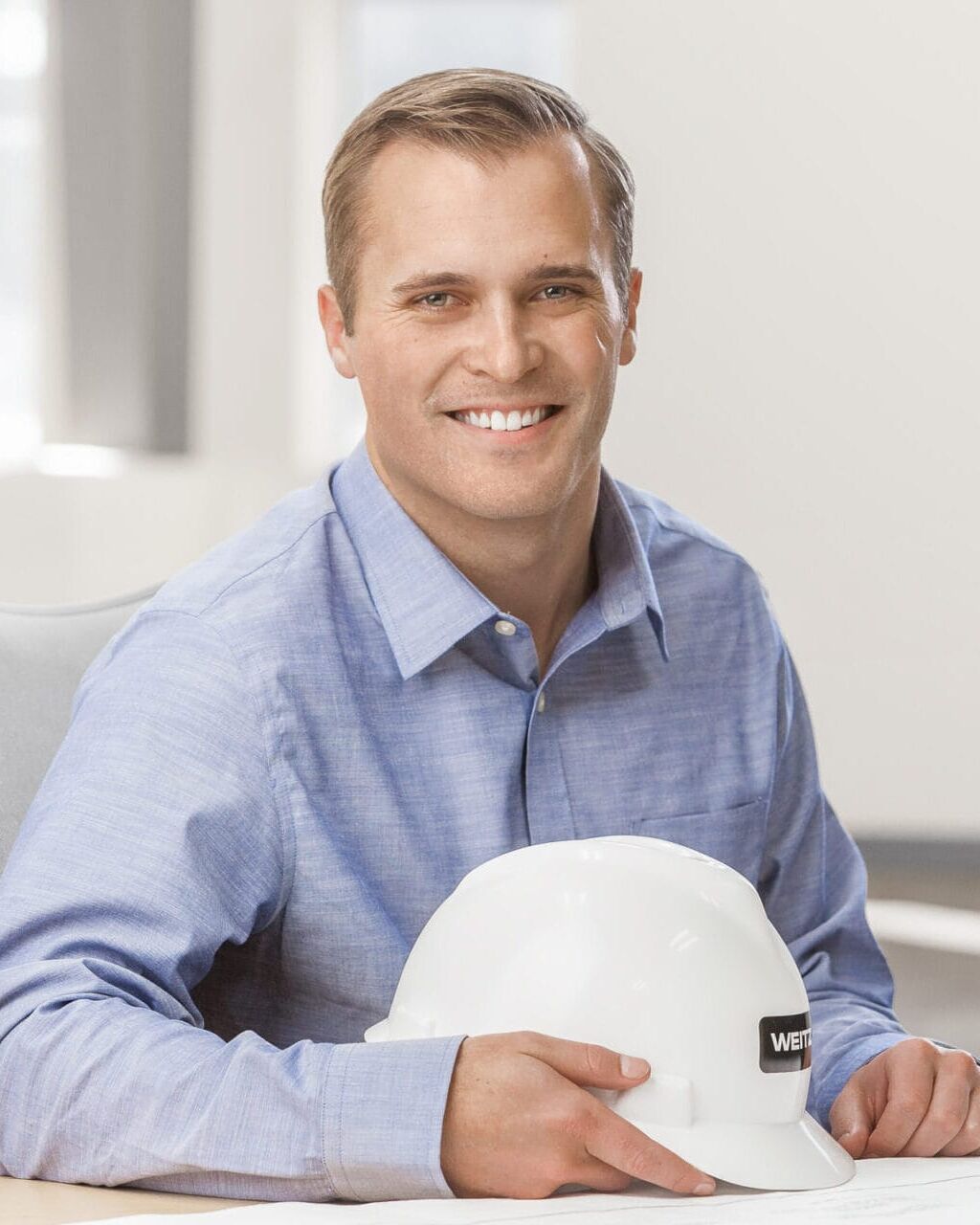 A man wearing a hard hat sitting at a desk for his professional headshot.