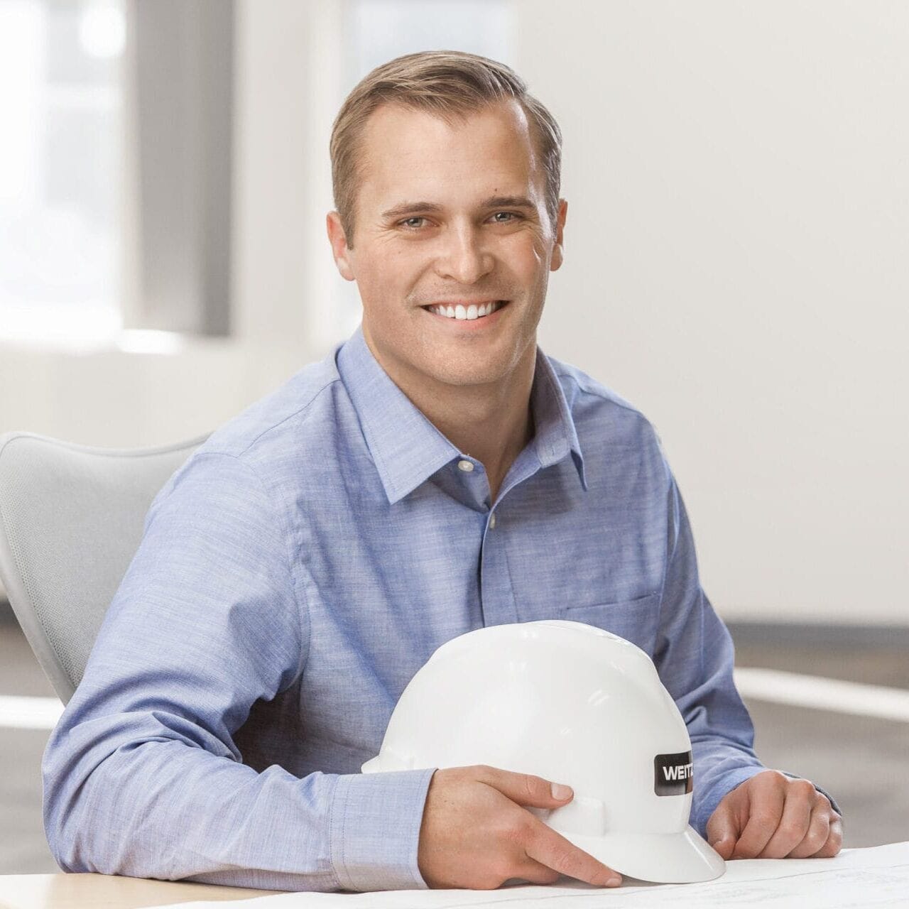 A man wearing a hard hat sitting at a desk for his professional headshot.