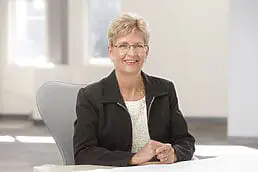 A woman in glasses sitting at a desk for her company headshot.