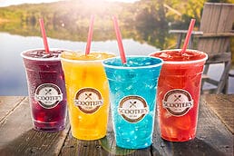 Four colorful drinks sitting on a wooden table next to a lake, captured in exquisite detail for food photography.