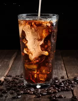 A glass of iced coffee is being poured into a glass for food photography.