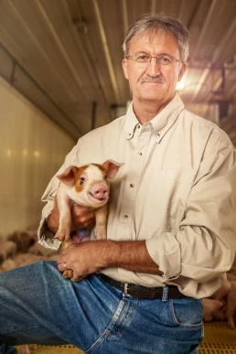A man holding a pig in a barn for a ag photography session.
