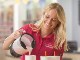 A woman pouring milk into a cup for food photography.