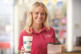 A blonde woman holding a cup of smoothie in a healthcare photography setting.