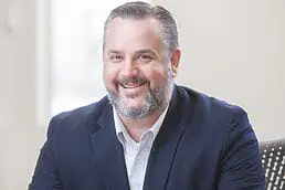 A smiling man in a suit sitting at a desk for a healthcare photography.
