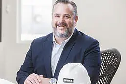 A man in a suit sitting at a desk with a hard hat for a healthcare photography session.