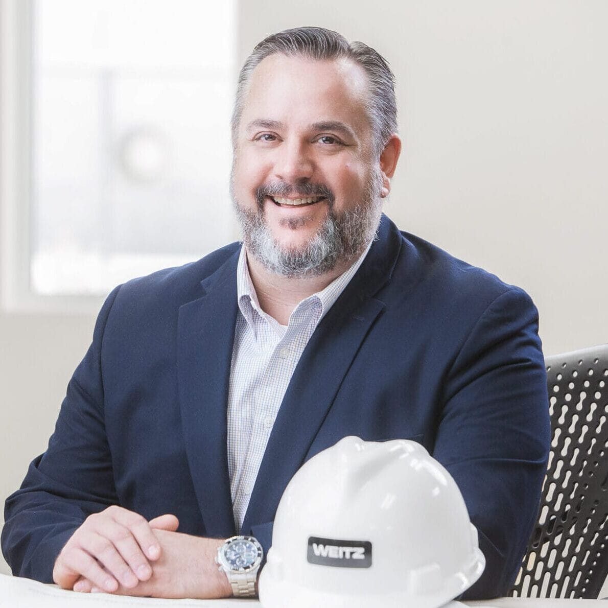 A man in a suit sitting at a desk with a hard hat for a healthcare photography session.