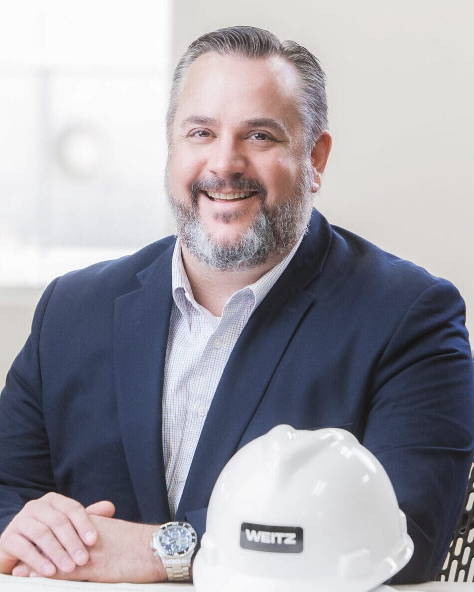 A man in a suit sitting at a desk with a hard hat for a healthcare photography session.