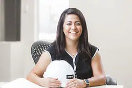 A woman wearing a hard hat sitting at a desk for her company headshot.