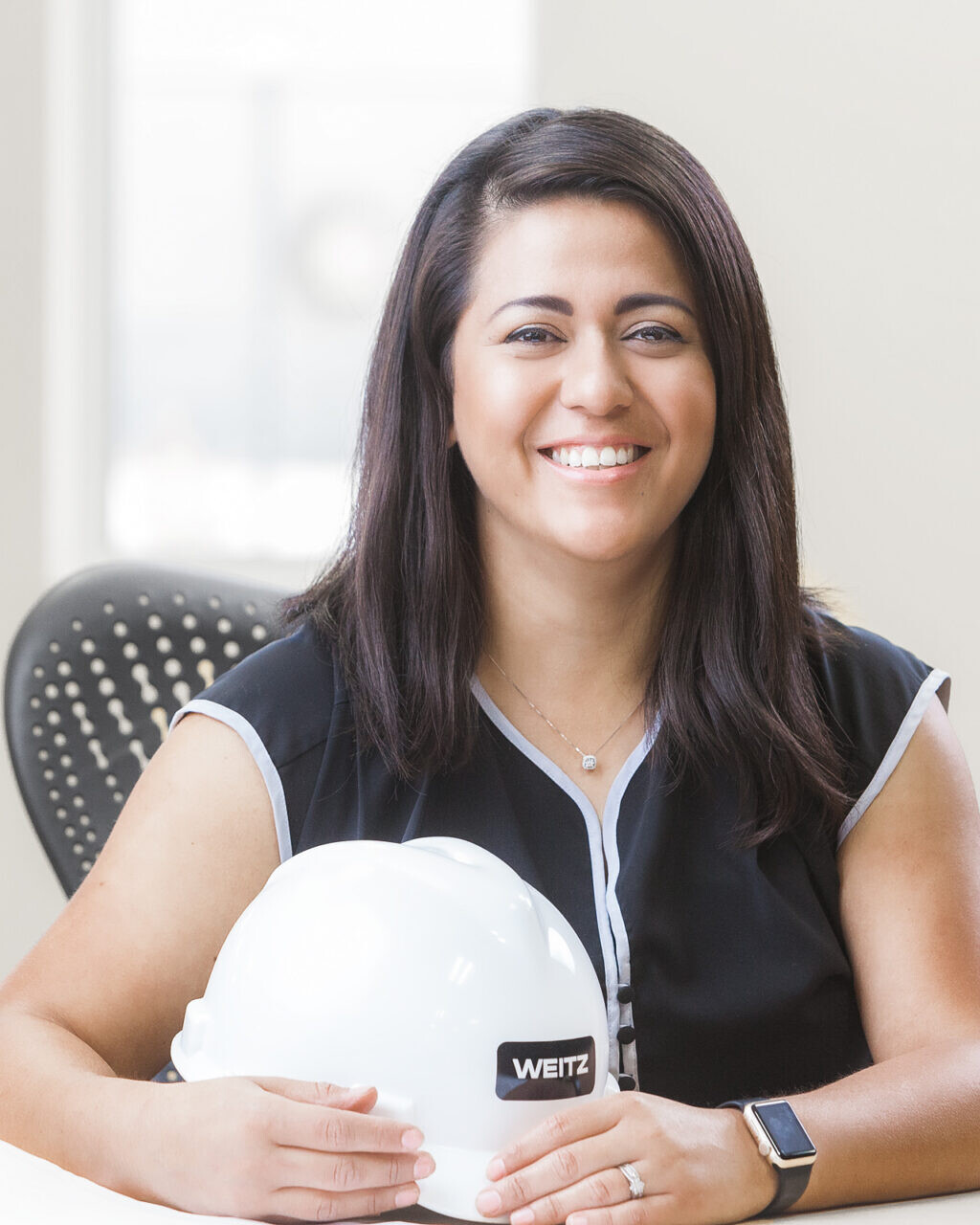 A woman wearing a hard hat sitting at a desk for her company headshot.