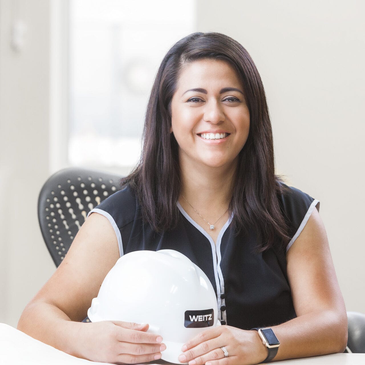 A woman wearing a hard hat sitting at a desk for her company headshot.