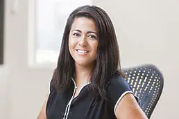 A woman in a black shirt sitting at a desk for her company headshot.