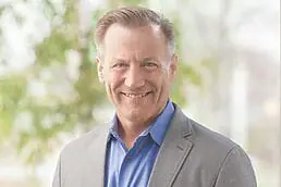 A smiling man in a gray suit and blue shirt poses for a headshot.