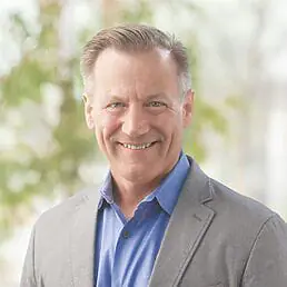A smiling man in a gray suit and blue shirt poses for a headshot.