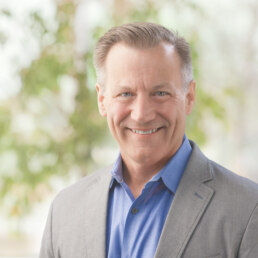 A smiling man in a gray suit and blue shirt poses for a headshot.