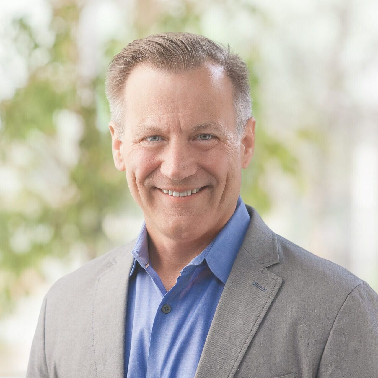 A smiling man in a gray suit and blue shirt poses for a headshot.