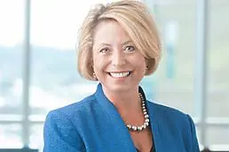 A smiling woman in a blue suit poses for her company headshot.