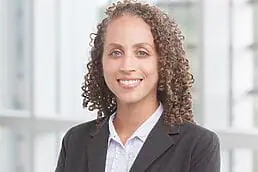A woman with curly hair wearing a suit in her headshot.